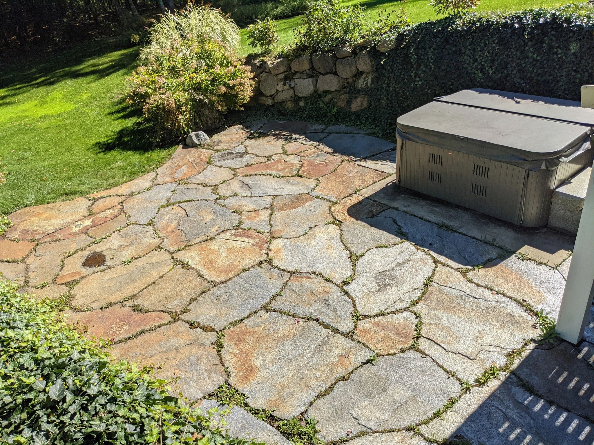 Stone patio with greenery and a covered hot tub in sunlight