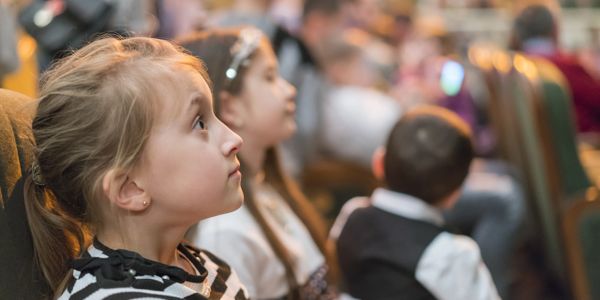 A young girl in an audience, wears a striped shirt. She intensely watches the stage in a theater.