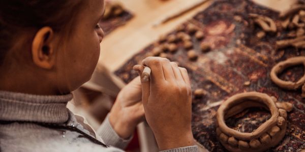 A young brown haired girl works with clay. She finishes the details, using coils.