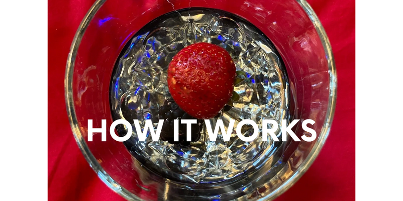 Small glass of water sitting on a small, black disc, with a strawberry and a blackberry in it.