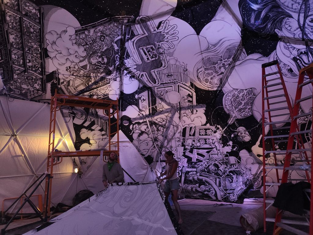 Two people install a large, intricate black and white mural inside a dome structure.