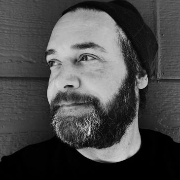 Black and white portrait of a bearded man wearing a beanie, looking thoughtfully to the side.