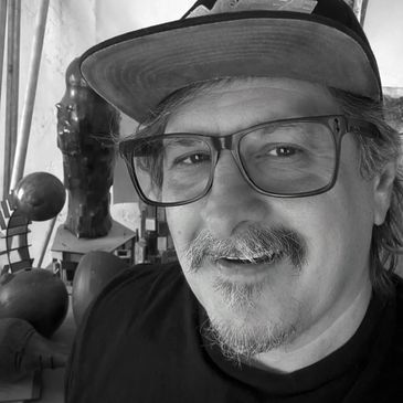 Smiling man wearing glasses and a cap in a room with sculptures.