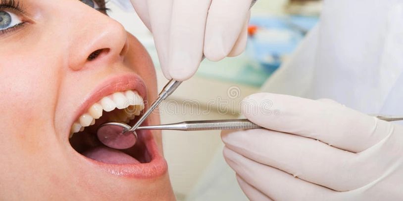 Dentist examining a patient’s open mouth with dental tools.