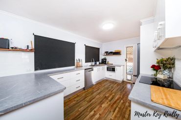 Modern kitchen with white cabinets and wooden flooring.