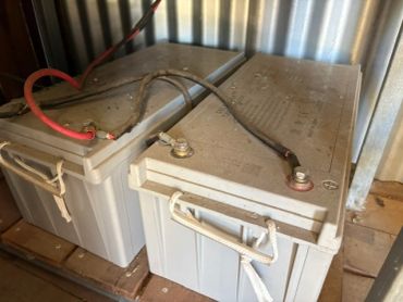 Two large batteries with connecting cables in a storage area.
