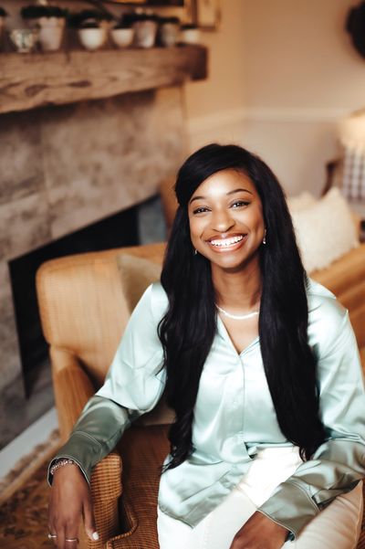 Smiling newborn care specialist in a satin blouse sitting comfortably in a cozy living room.