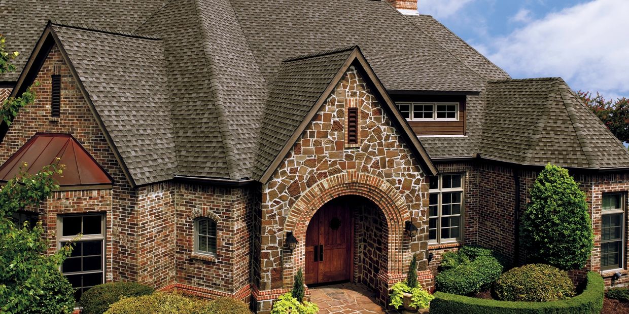 Elegant brick house with intricate roof and lush landscaping.