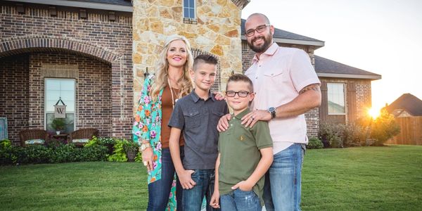 Happy family of four posing outside their brick house at sunset.