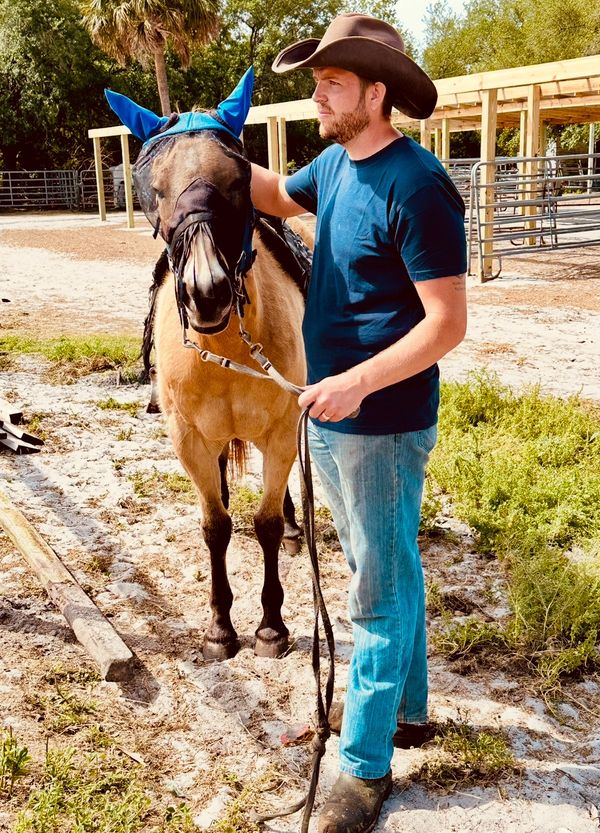 Matt The Welder standing beside a horse wearing a blue fly mask in Florida. Cowboy