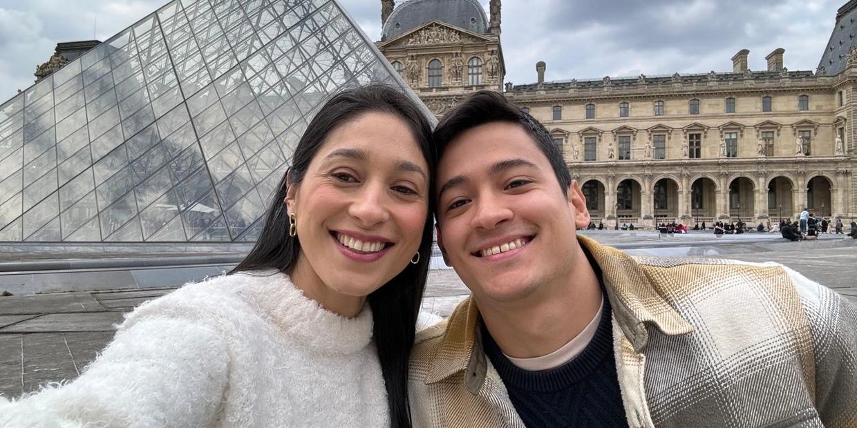 A happy couple taking a selfie in front of the Louvre Pyramid in Paris.