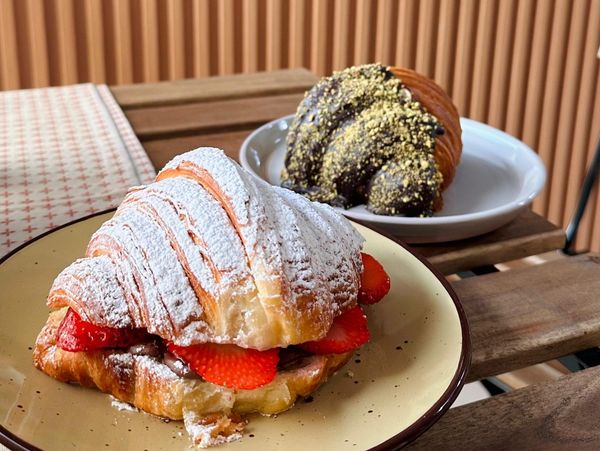 Two delicious croissants, one with strawberries and powdered sugar, the other with chocolate and crushed nuts.