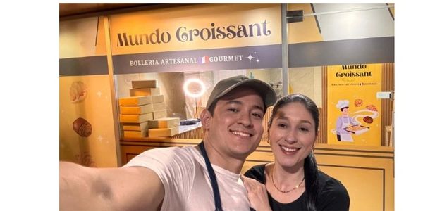 Two smiling individuals taking a selfie in front of Mundo Croissant bakery.