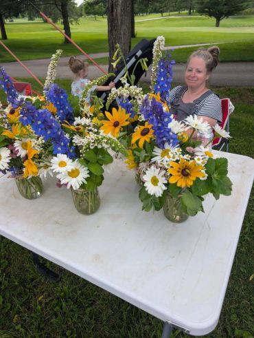 Colorful flower bouquets on a table with a woman smiling.
