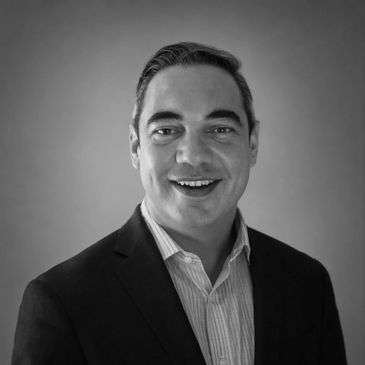 Black and white portrait of a smiling man in a suit jacket and striped shirt.