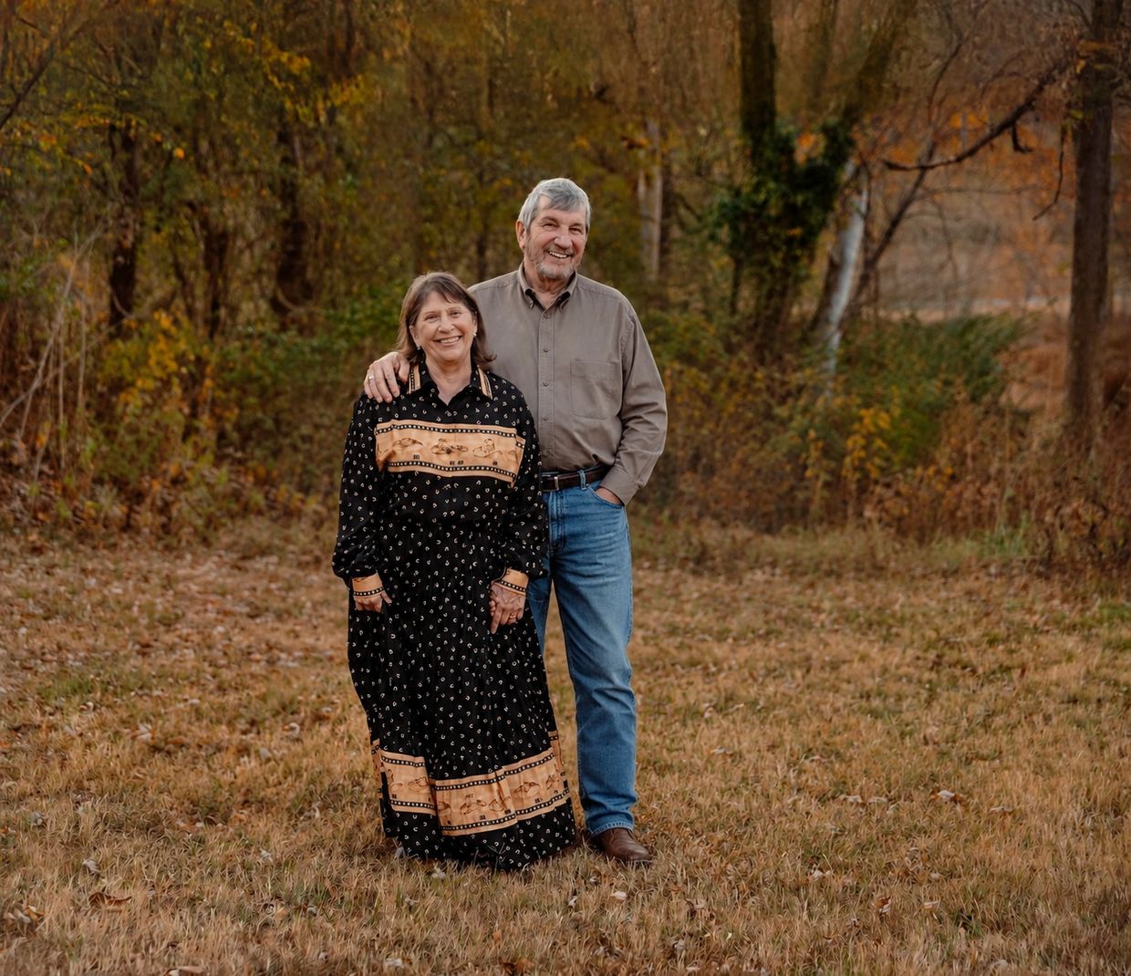 Happy elderly couple standing together in a fall forest clearing.