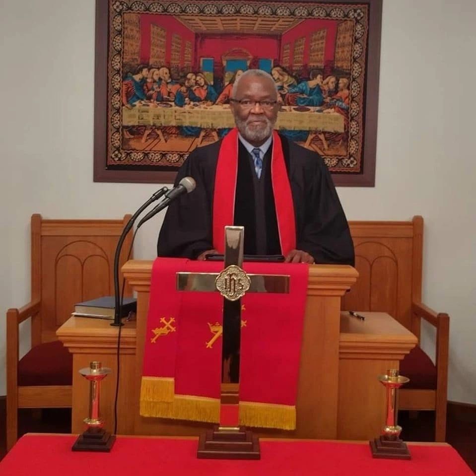 Minister standing at pulpit with cross and Last Supper painting.