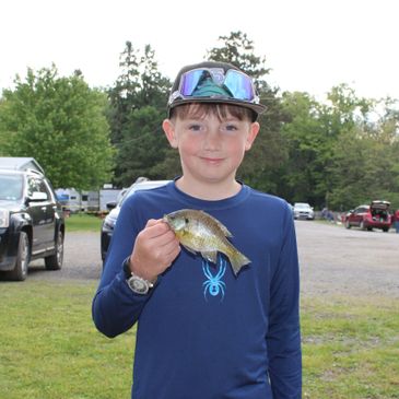 Boy holding a small fish with a smile outdoors.