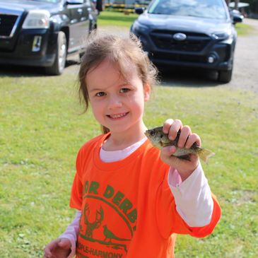 Smiling girl holding a small fish outdoors on a sunny day.