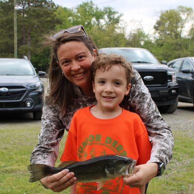 Smiling woman and boy holding a fish they caught outdoors.