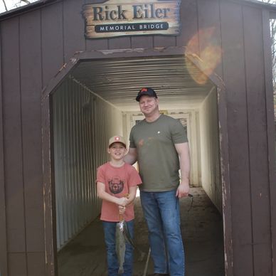 A man and a boy stand under the Rick Eiler Memorial Bridge holding a fish.