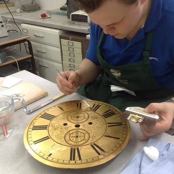 Applying gold leaf to a worn section of a clock dial.