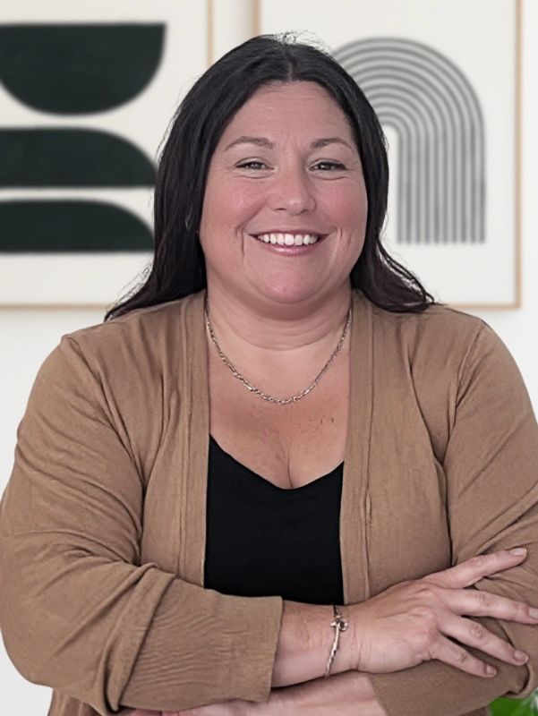 Smiling woman with arms crossed, wearing a brown cardigan and black top.