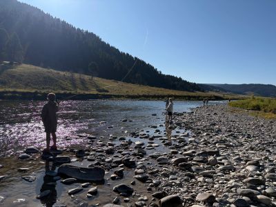People standing and fishing by a rocky river under a clear blue sky.