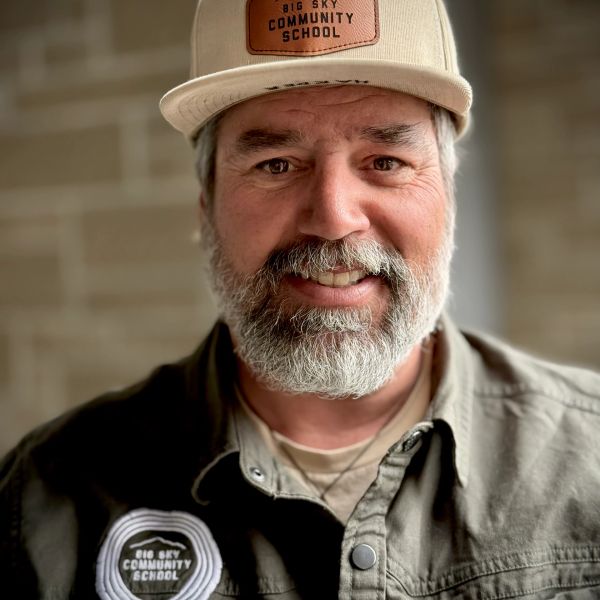 Smiling man wearing a Big Sky Community School hat and shirt.