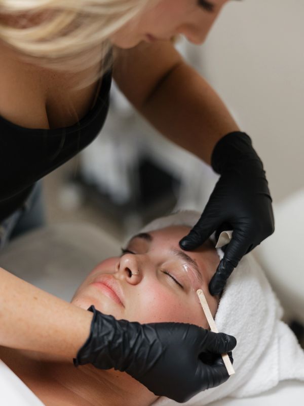 Woman receiving eyebrow waxing treatment.