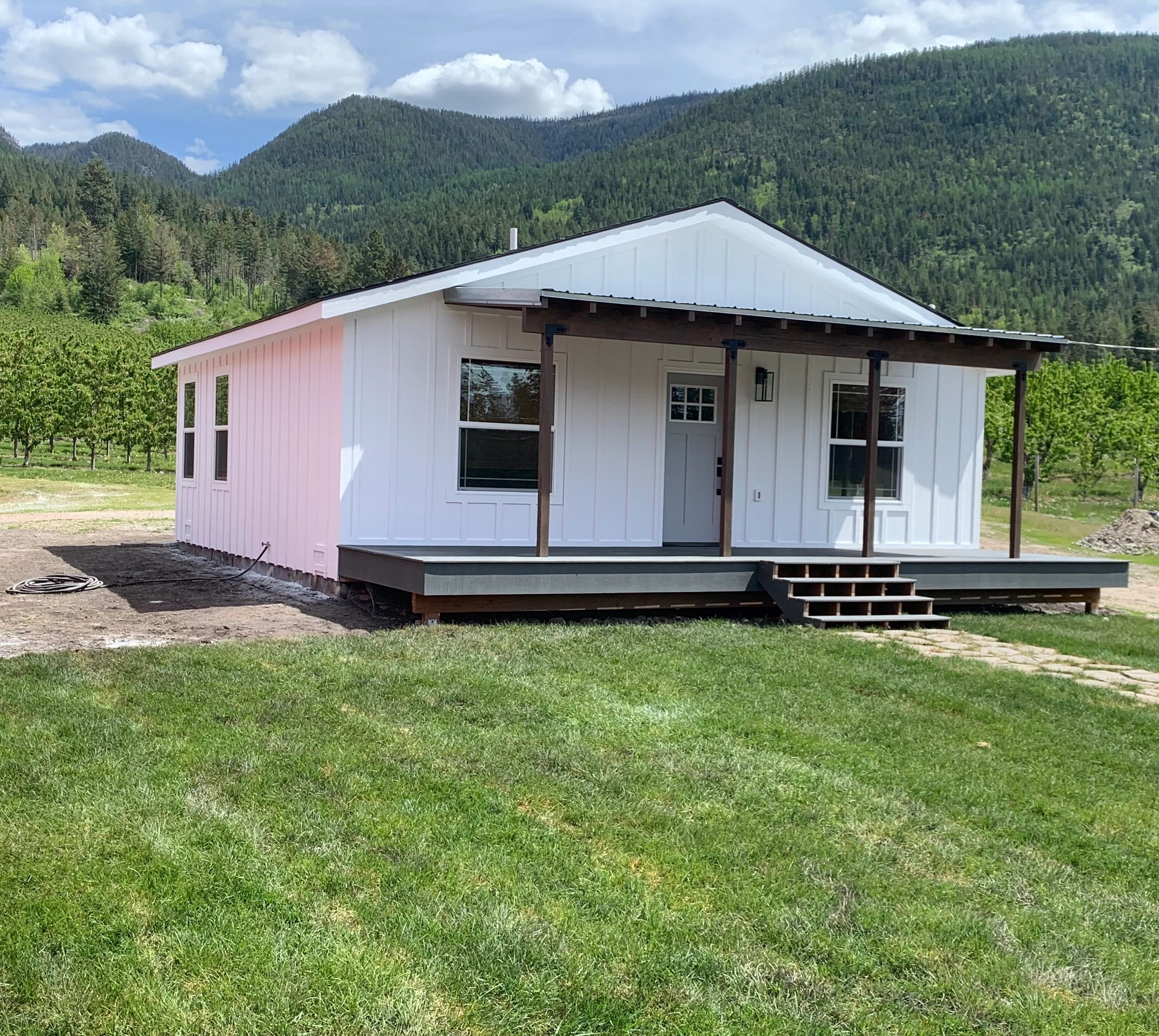 A small white house with a front porch in a lush green mountainous area.
