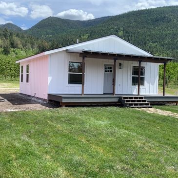 Small white cabin with porch in green mountainous landscape.