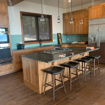Modern kitchen with wooden cabinets, black countertops, and four bar stools at the island.