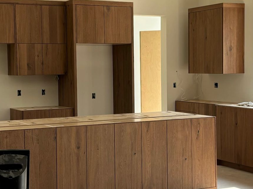 Modern kitchen under construction with wooden cabinets and large window.