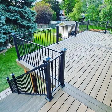Spacious wooden deck with black metal railings overlooking a green backyard.