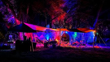 Colorful illuminated tents set up in a forest at night.