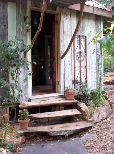Rustic wooden steps lead to a cozy cabin entrance surrounded by plants.
