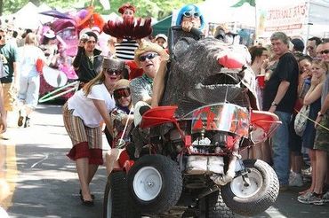 People participating in a quirky parade with a rat-themed vehicle.