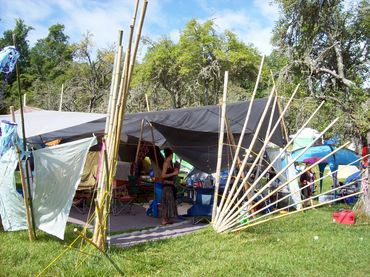 Outdoor campsite with bamboo structures and tarps under a sunny sky.
