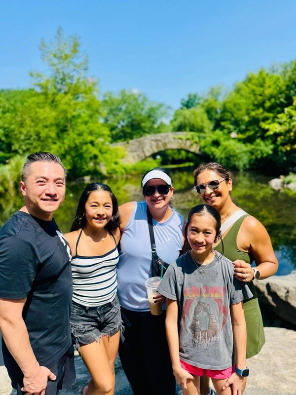 Family enjoying a sunny day outdoors by a scenic stone bridge and river.