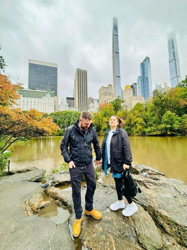 Couple holding hands near a lake with city skyscrapers in the background.