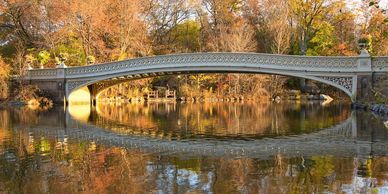 Elegant arched bridge reflecting on calm water amid autumn foliage.