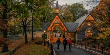 People walking near a charming autumn chapel in a park.