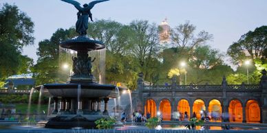 Evening view of a lit fountain and historic building in a park setting.