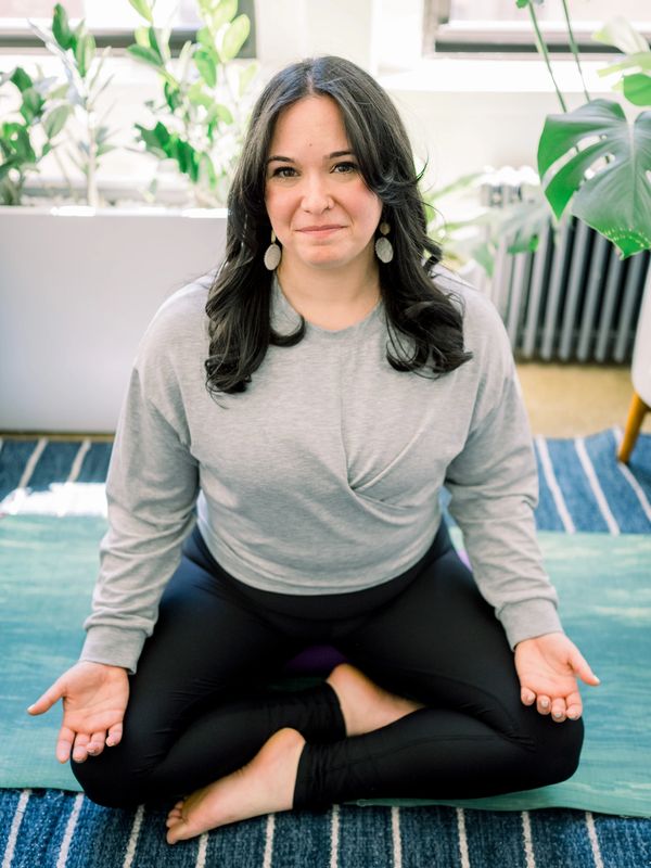 Woman meditating cross-legged on a yoga mat indoors.
