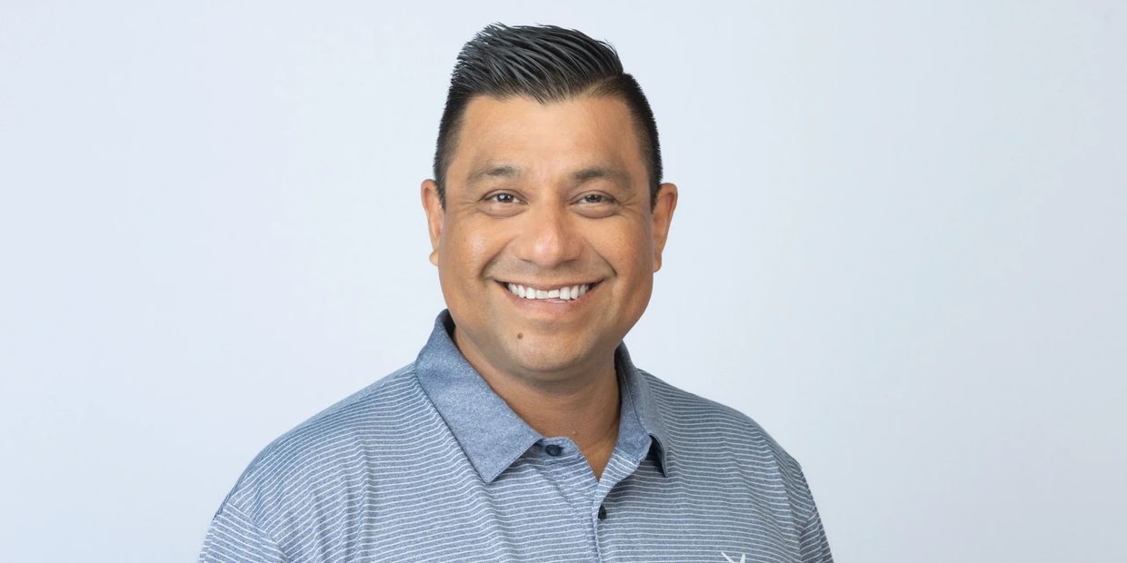 Smiling man in striped polo shirt against plain background.