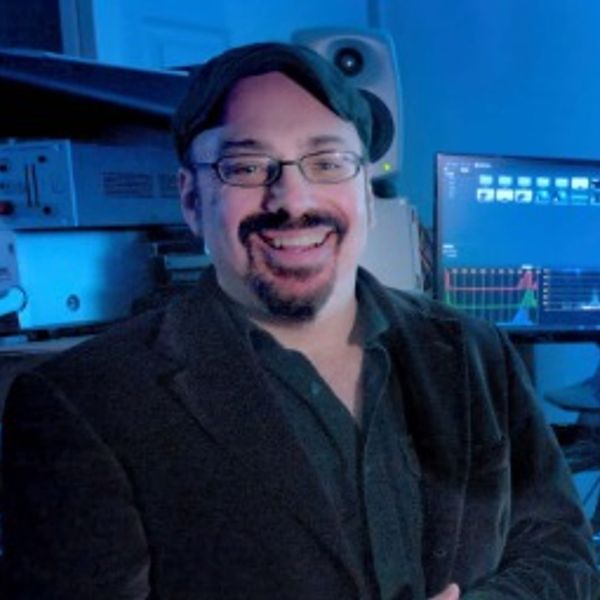 Man with glasses and cap smiling in a blue-lit studio.