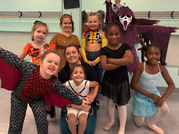 A group of children and an adult in costumes posing in a dance studio.