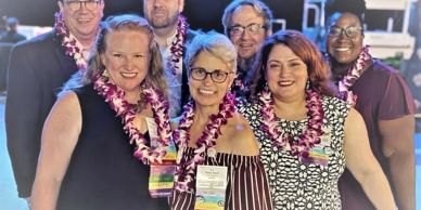 Group of smiling people wearing leis at an event.