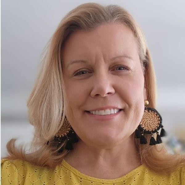 Smiling woman wearing large woven earrings and a yellow top.